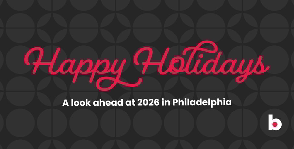 Holiday graphic with red script text reading ‘Happy Holidays’ on a dark patterned background. Below, white text says ‘A look ahead at 2026 in Philadelphia.’ A small ‘b’ logo appears in the bottom right corner.