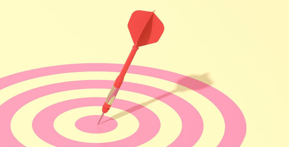 A red dart is stuck in the bullseye of a pink target on a pale yellow background.