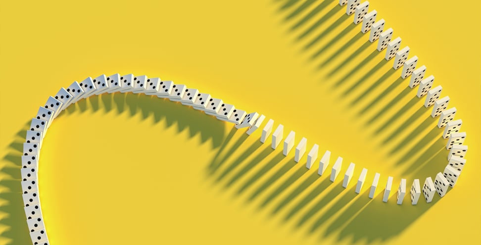 A curved line of standing dominoes casts shadows on a bright yellow background.